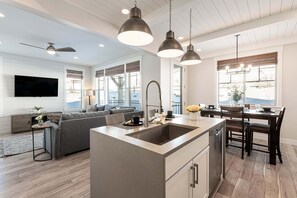 Et moderne køkken med en central ø, spiseområde med stole, og en stue med sofa.