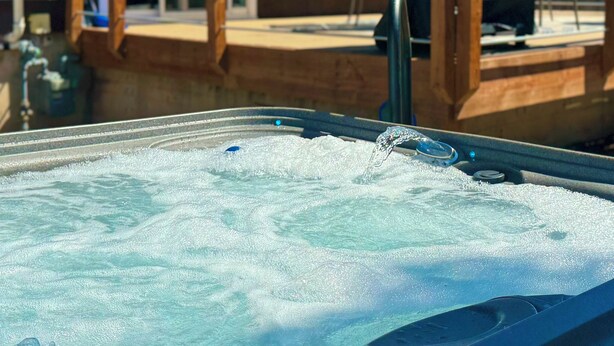A hot tub with water bubbling, surrounded by wooden deck and chairs. - ᨒ Hot Tub / Fire Pit / Game Lounge / Fenced Yard ᨒ (Colorado Springs)