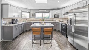 Een moderne keuken met grijze kastjes, roestvrijstalen apparatuur en een centraal eiland met twee barkrukken.