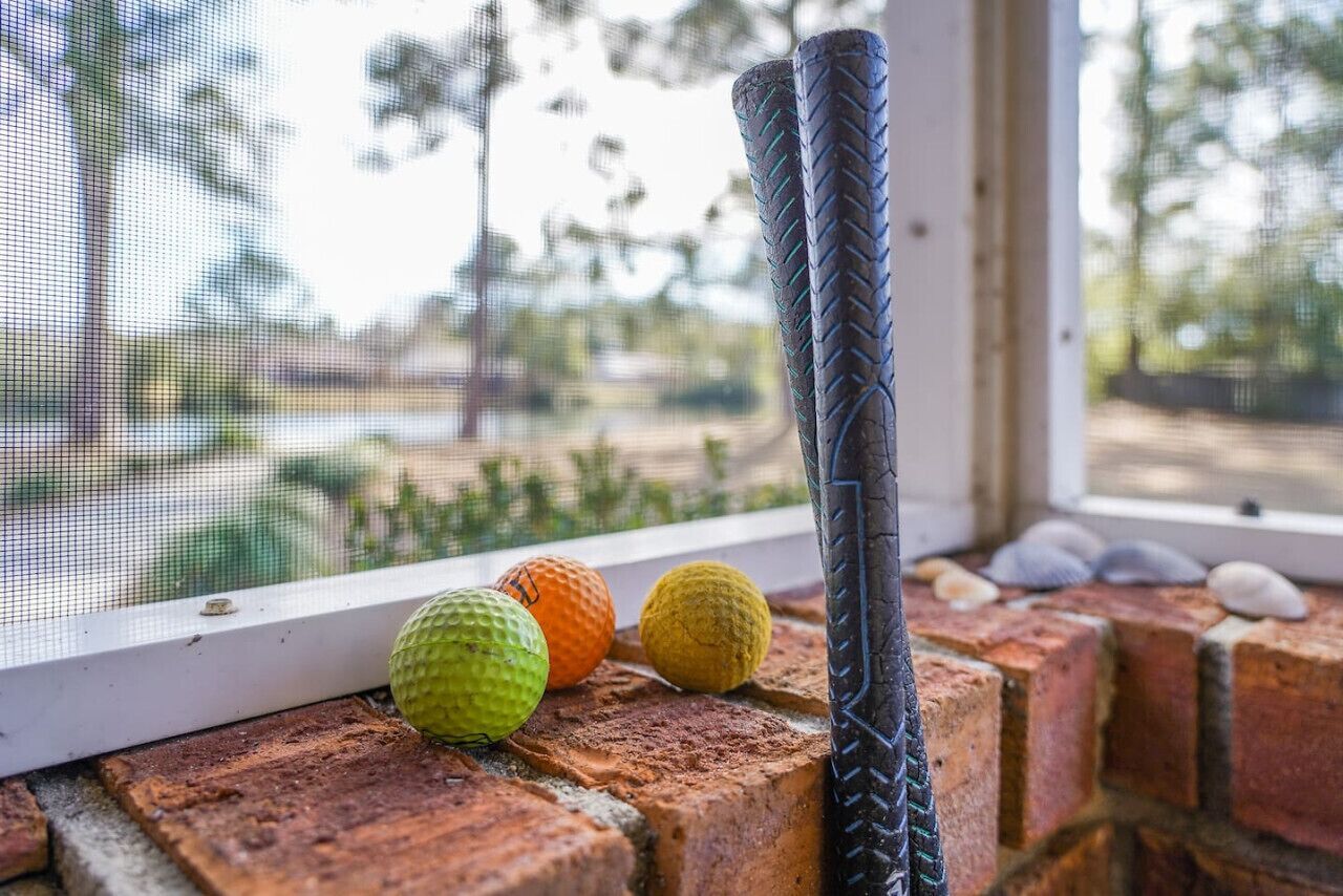 Una ventana con vista a un muro de ladrillo, dos palos de golf y tres pelotas de golf sobre el alféizar.