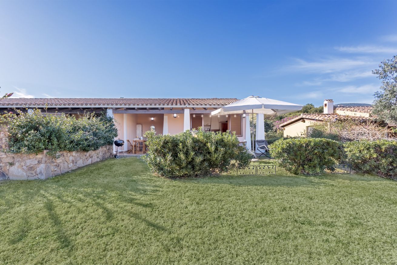 A house with a covered patio, a lawn, and a stone wall.