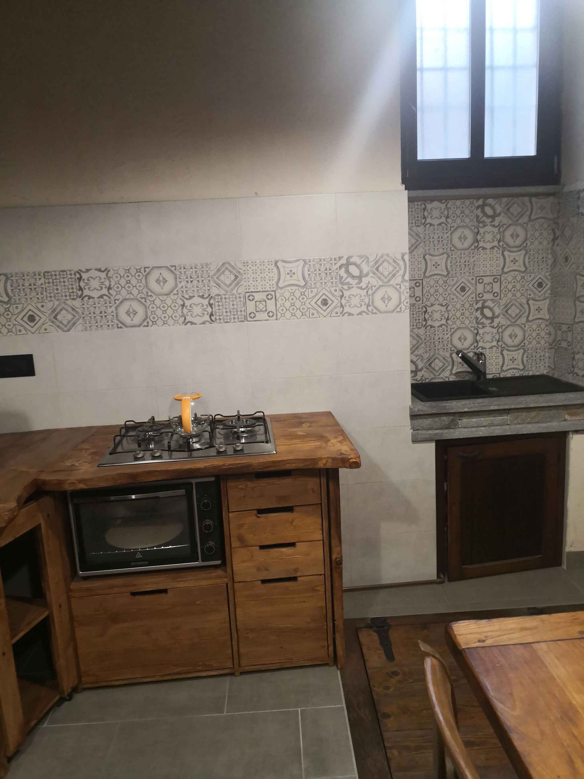 Une cuisine compacte équipée d’une cuisinière à gaz, d’un four à micro-ondes et d’un évier. Les murs sont décorés de carreaux à motifs.