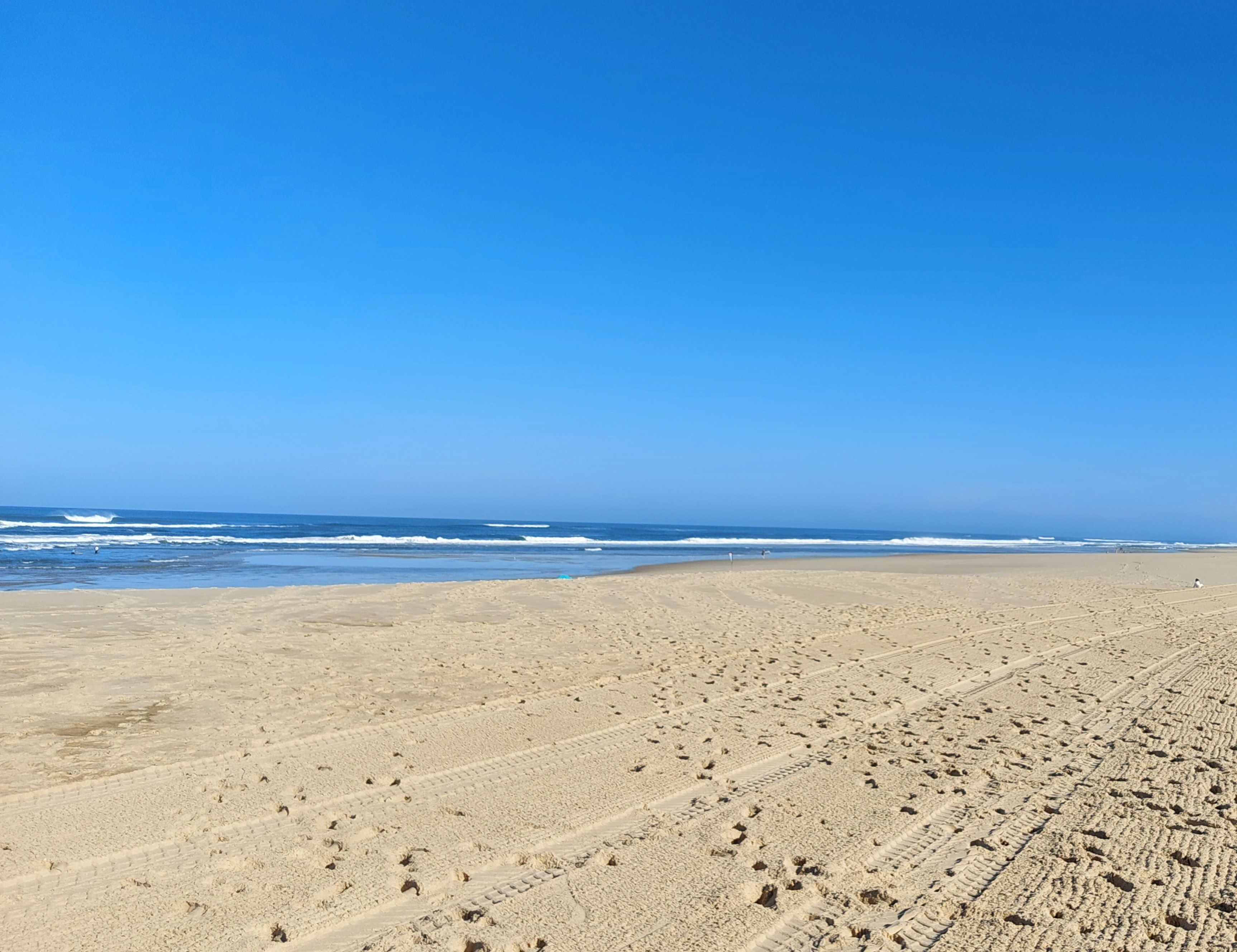 Una amplia playa arenosa con marcas de neumáticos y huellas visibles.