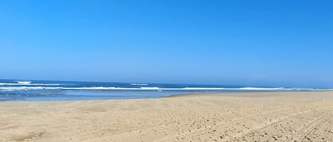 Una amplia playa arenosa con marcas de neumáticos y huellas visibles.