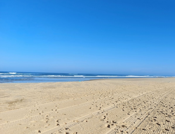 A wide sandy beach with visible tire tracks and footprints.