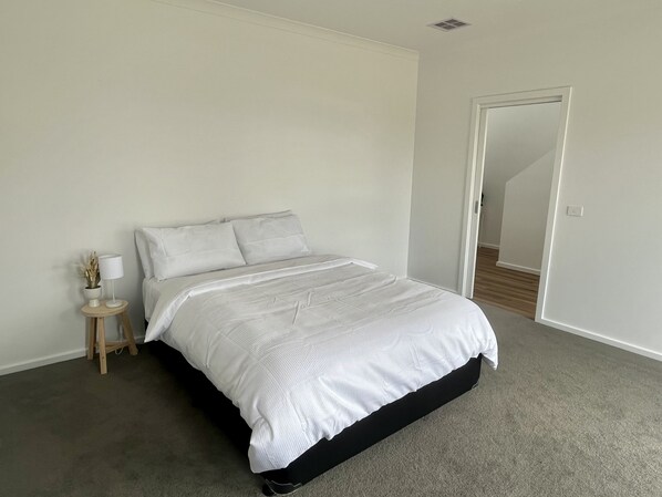 A bedroom with a bed, a bedside table with a lamp, and a door leading to another room.