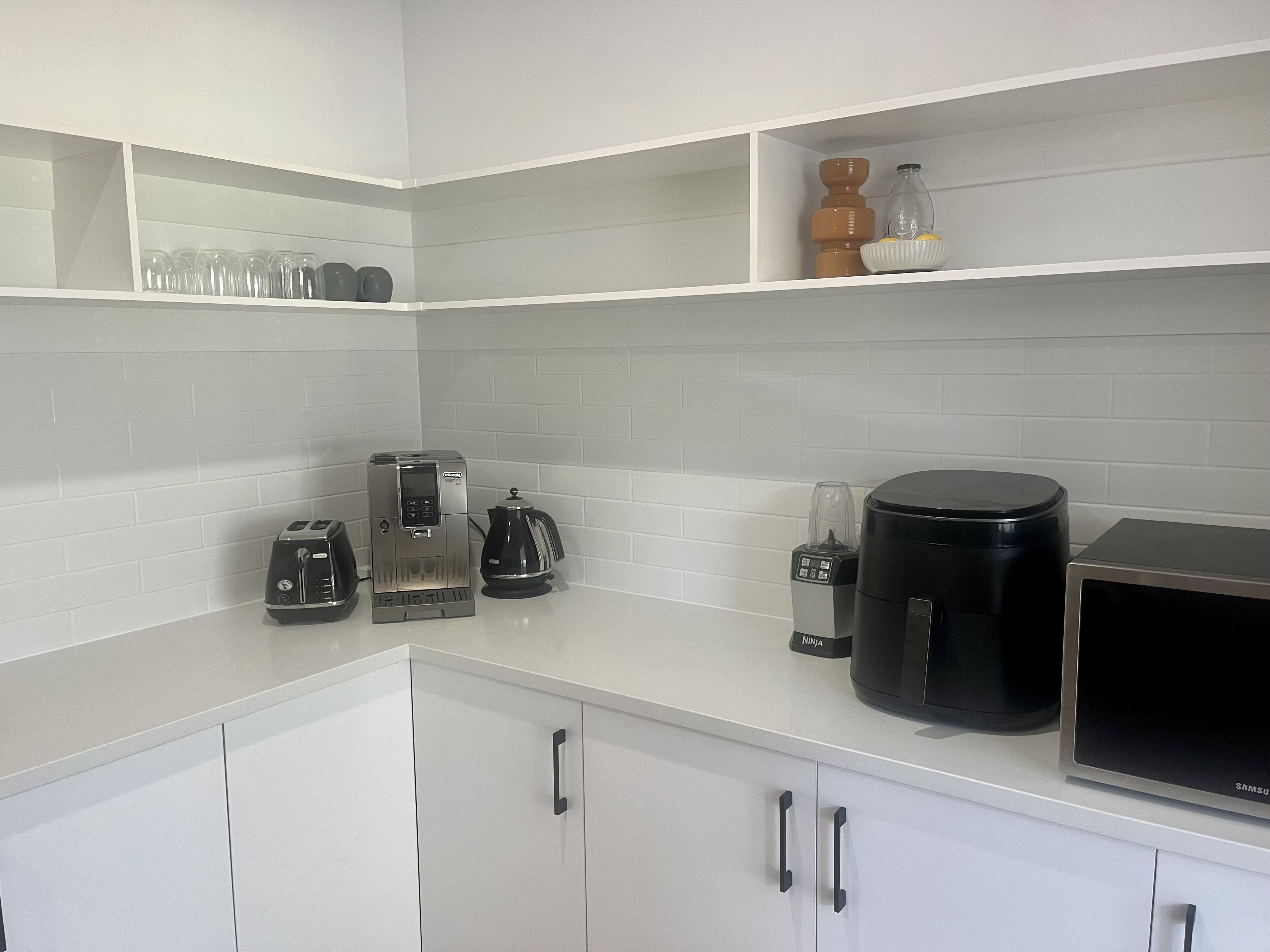 Une cuisine moderne avec des meubles blancs, une machine à café intégrée, un grille-pain et un four à micro-ondes.