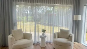 Una habitació amb dues butaques beix, una taula petita blanca amb una planta, i una làmpada de peu.