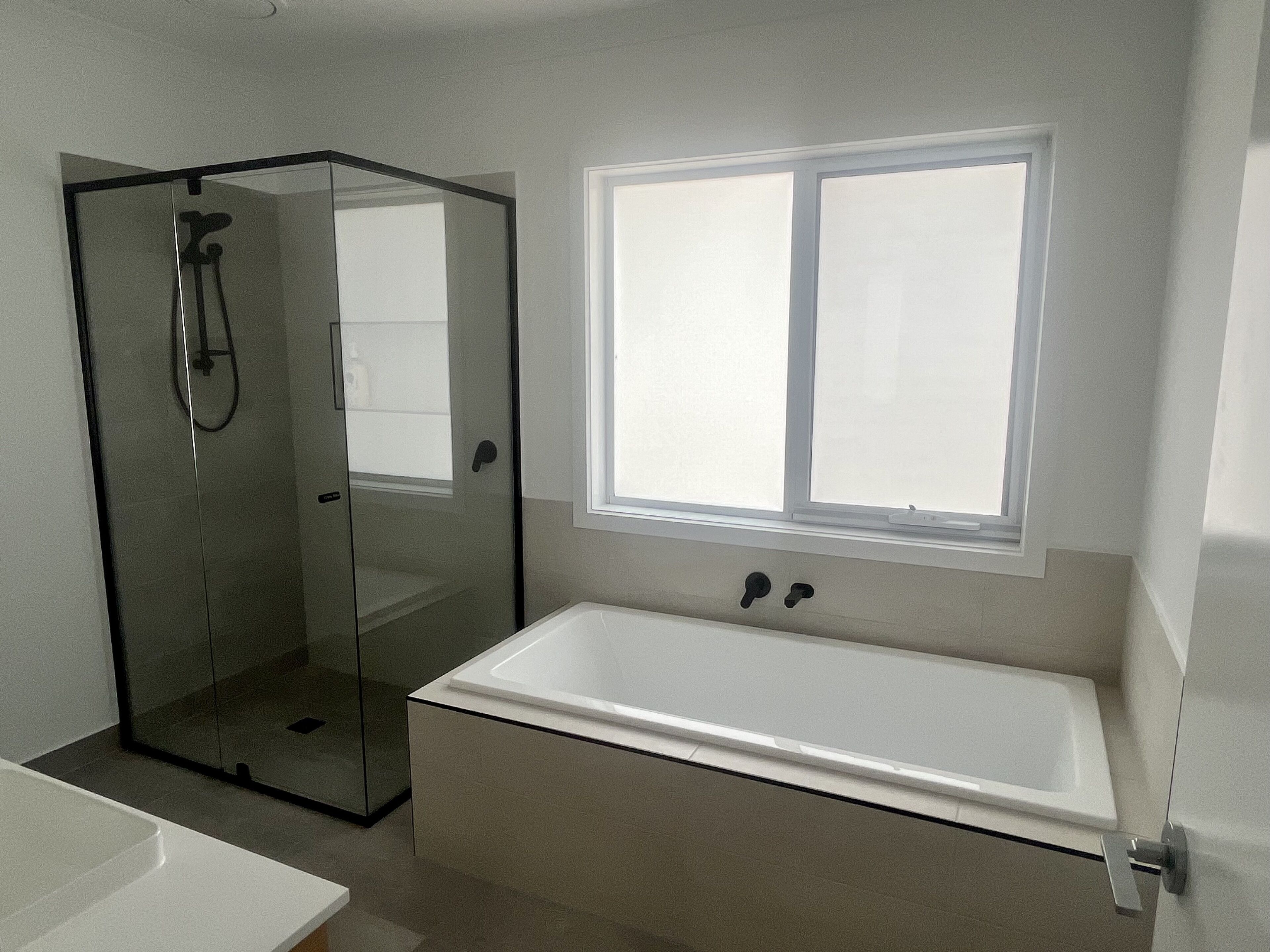 A modern bathroom with a glass-enclosed shower, a large bathtub, and a window providing natural light.