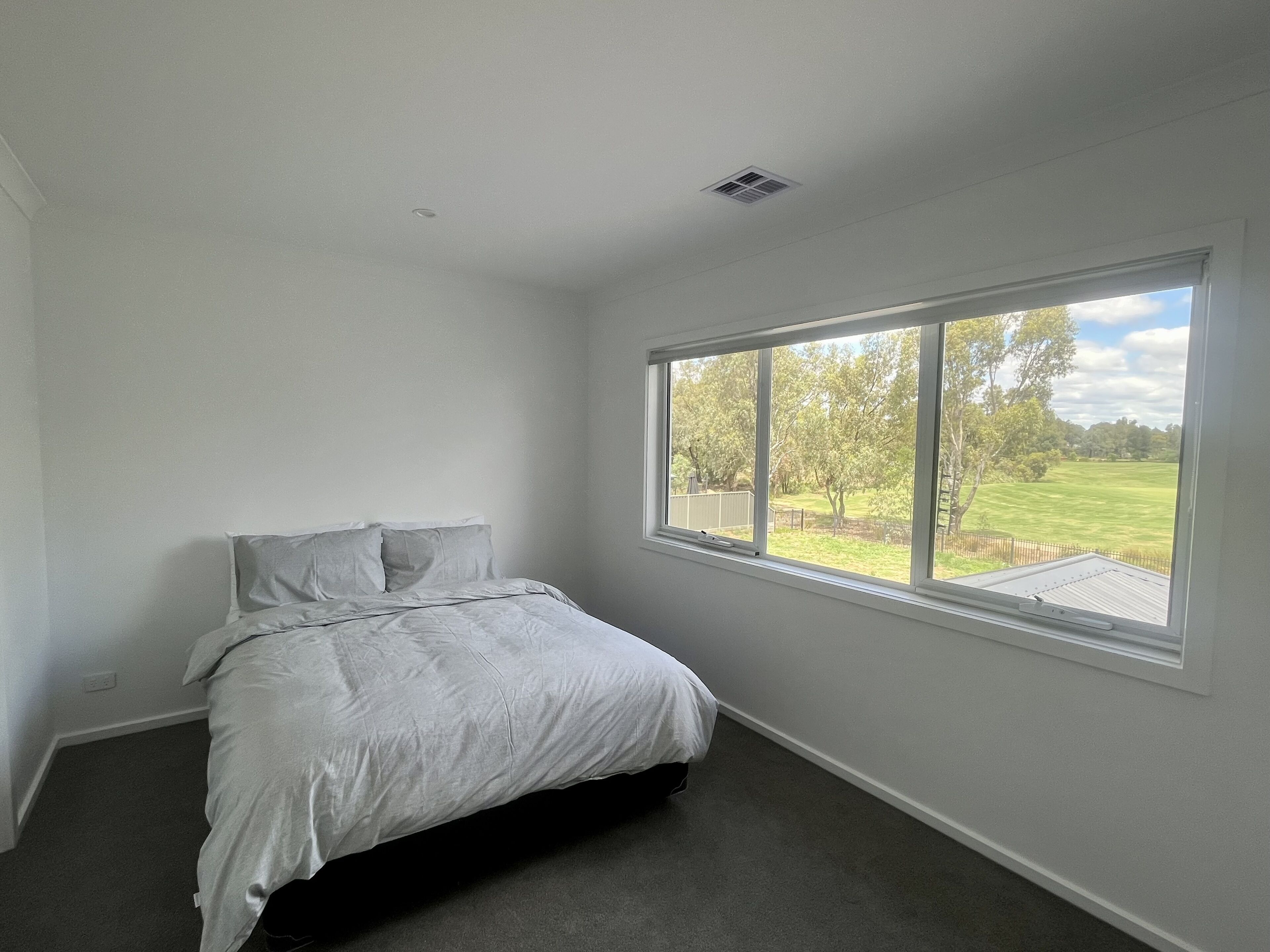 A bedroom with a large window, a bed, and a ceiling vent.