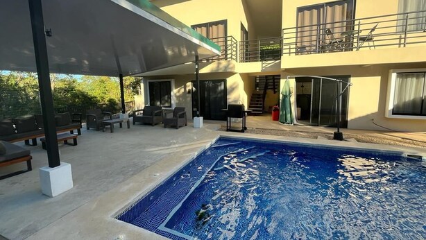 Um edifício de dois andares com piscina, área de estar ao ar livre e um pátio coberto.
