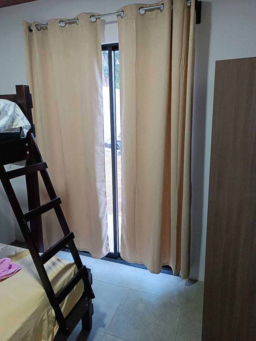 A room with a bunk bed, a wooden ladder, beige curtains, and a window.