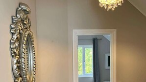 Un couloir agrémenté d’un miroir décoratif, d’une plante en pot et d’un lustre.