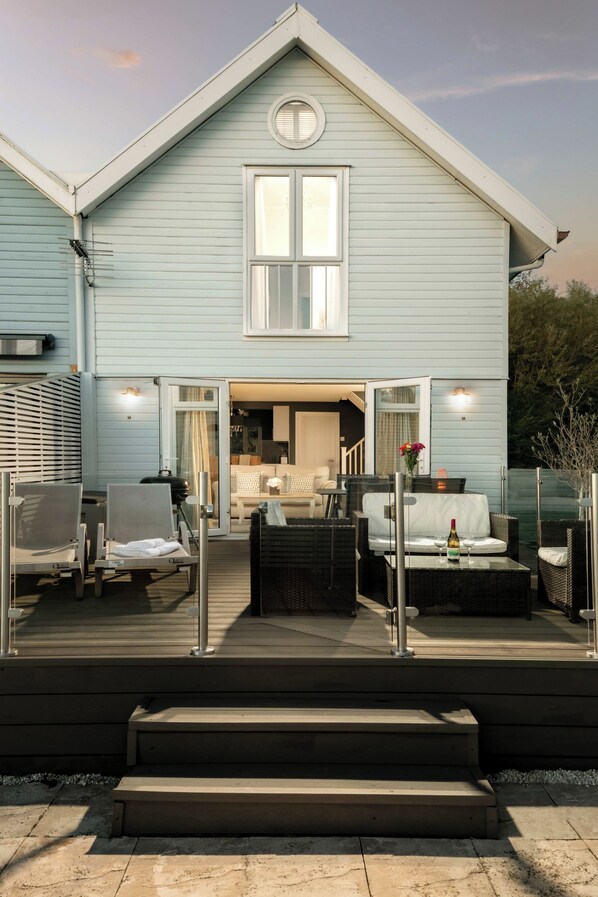 A light blue two-story house with a covered patio area featuring outdoor furniture and a grill.