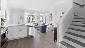 Eine geräumige Küche mit weißen Schränken, einer zentralen Kochinsel und einem Essbereich mit blauem Stuhl und weißem Sofa.