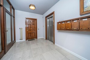 A hallway with a wooden door, an elevator, and a wall-mounted storage unit. - GuestHost - Udine's Heart Apartment (Udine)
