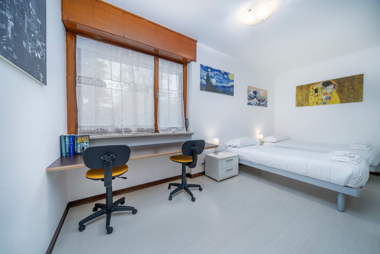 A bedroom with a single bed, a desk with two chairs, a nightstand, and wall art.