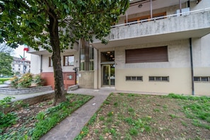 Un bâtiment à l’architecture moderne, doté d’une grande entrée, d’un arbre au premier plan et d’une zone pavée avec de l’herbe.