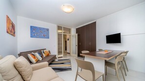 A modern living room with a sofa, a dining table, chairs, a TV, and artwork on the walls. - GuestHost - Udine's Heart Apartment (Udine)