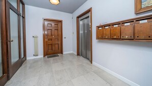 A hallway with a wooden door, an elevator, and a wall-mounted storage unit. - GuestHost - Udine's Heart Apartment (Udine)