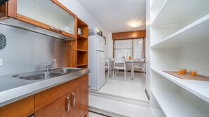 A compact kitchen with a double sink, a refrigerator, and a dining area with a table and chairs. - GuestHost - Udine's Heart Apartment (Udine)