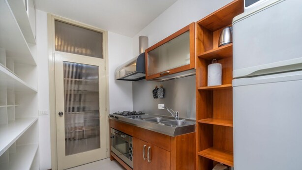 A compact kitchen with a gas stove, oven, and stainless steel sink. There are wooden shelves and a refrigerator. - GuestHost - Udine's Heart Apartment (Udine)