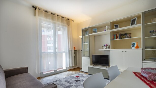 Ein modernes Wohnzimmer mit einer Couch, einem Esstisch, einem Fernseher und einem Bücherregal.