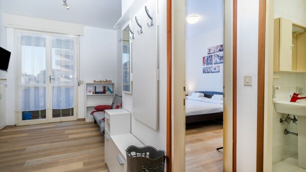 Un dormitorio moderno con cama, escritorio, silla, armario y baño con lavamanos.