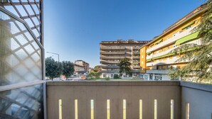 Un balcón con vista a un edificio de varios pisos, una pared de concreto y una barandilla metálica.