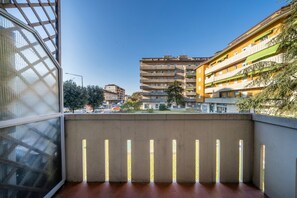 A balcony with a view of a multi-story building, a concrete wall, and a metal railing.