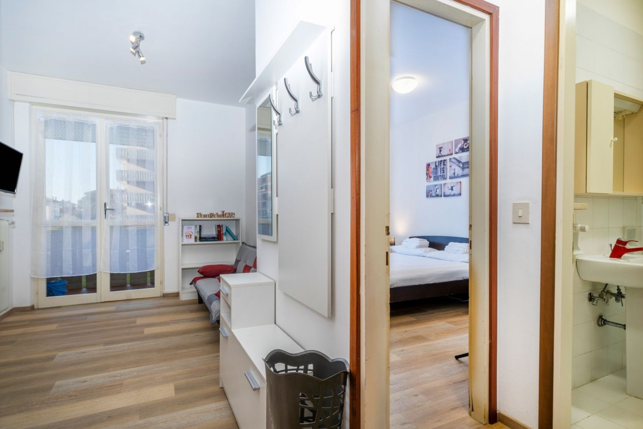 A modern bedroom with a bed, a desk, a chair, a wardrobe, and a bathroom with a sink.