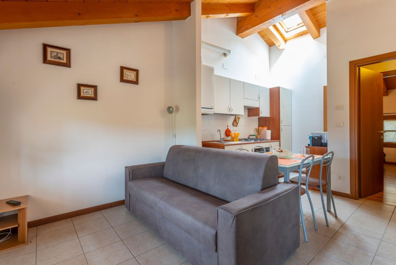 Un espacio de sala acogedor con sofá, una mesa de comedor con sillas, una cocina al fondo y un tragaluz arriba.