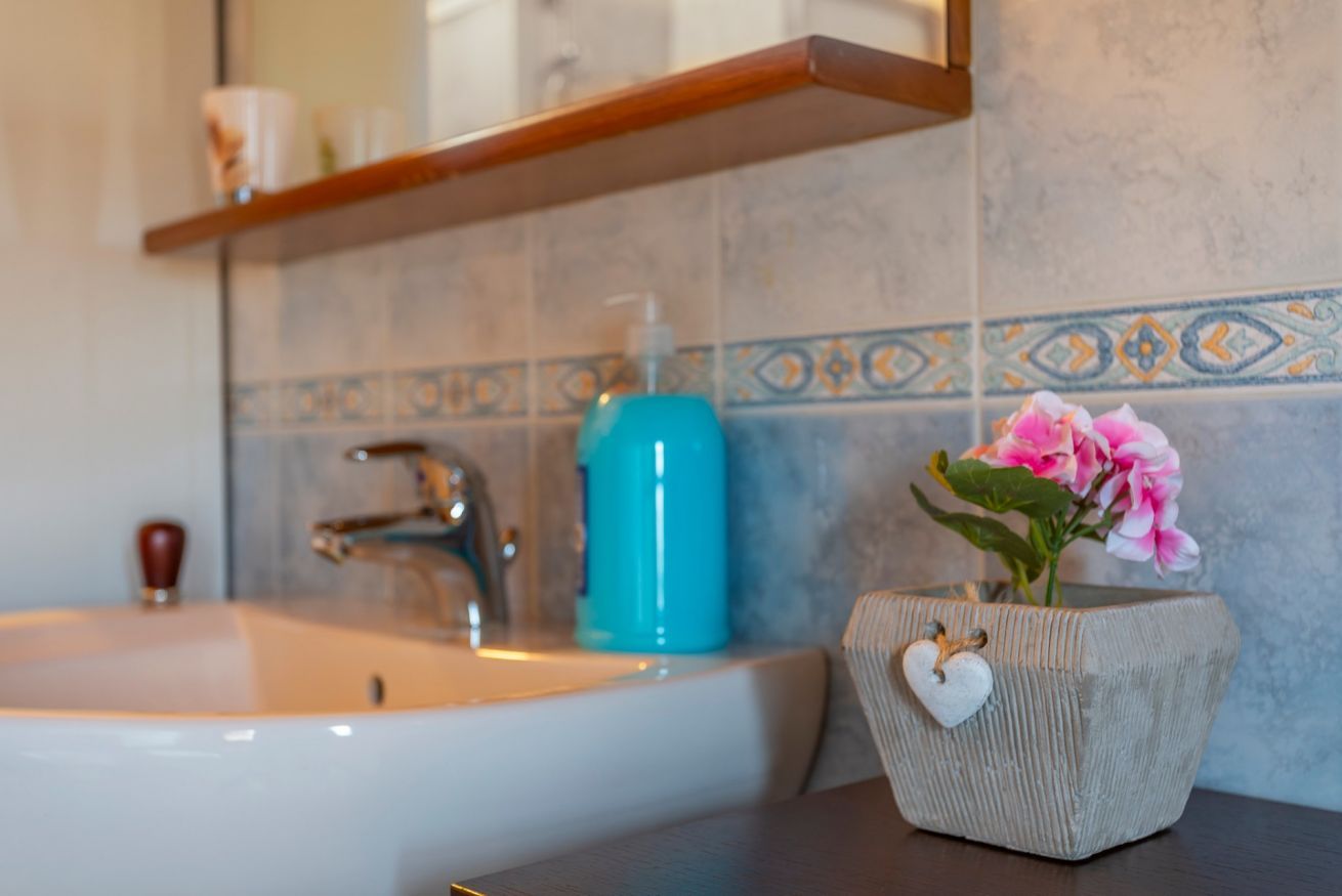 Een badkamer met een wit wastafel, een blauwe zeepdispenser en een decoratieve vaas met bloemen.