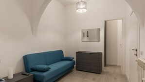 Une chambre à coucher moderne avec un canapé bleu, une table de chevet avec une lampe, une commode et un luminaire suspendu.