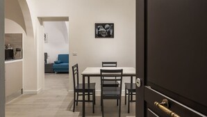 Un coin repas avec une table et des chaises, une porte sombre et un canapé bleu à l’arrière-plan.