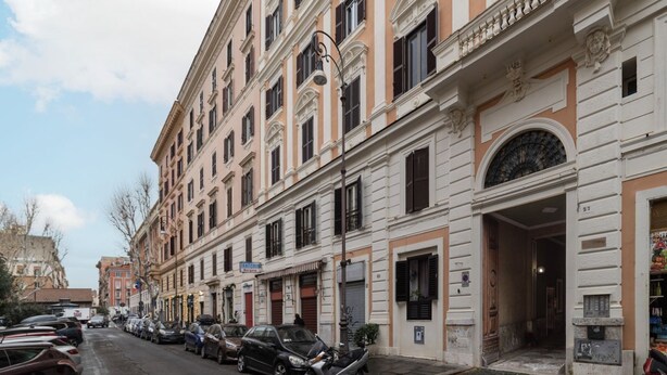 Une rangée de bâtiments européens classiques aux façades uniformes, avec des voitures garées et un ciel dégagé.