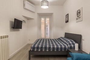 A bedroom with a bed, a TV, a radiator, and a window.