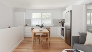 Een moderne keuken met witte kasten, een houten eettafel en een grijze bank.