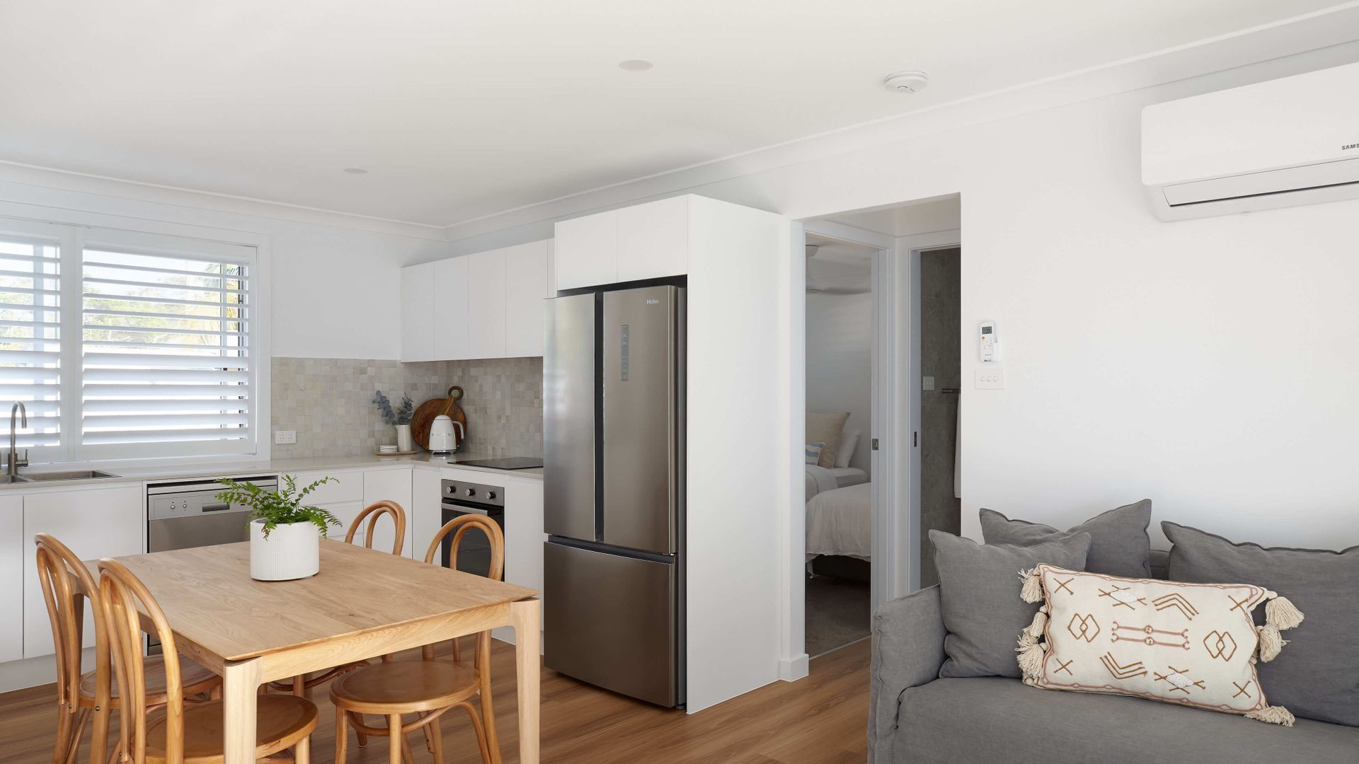 A modern kitchen with white cabinetry, a stainless steel refrigerator, and a dining area with a wooden table and chairs.