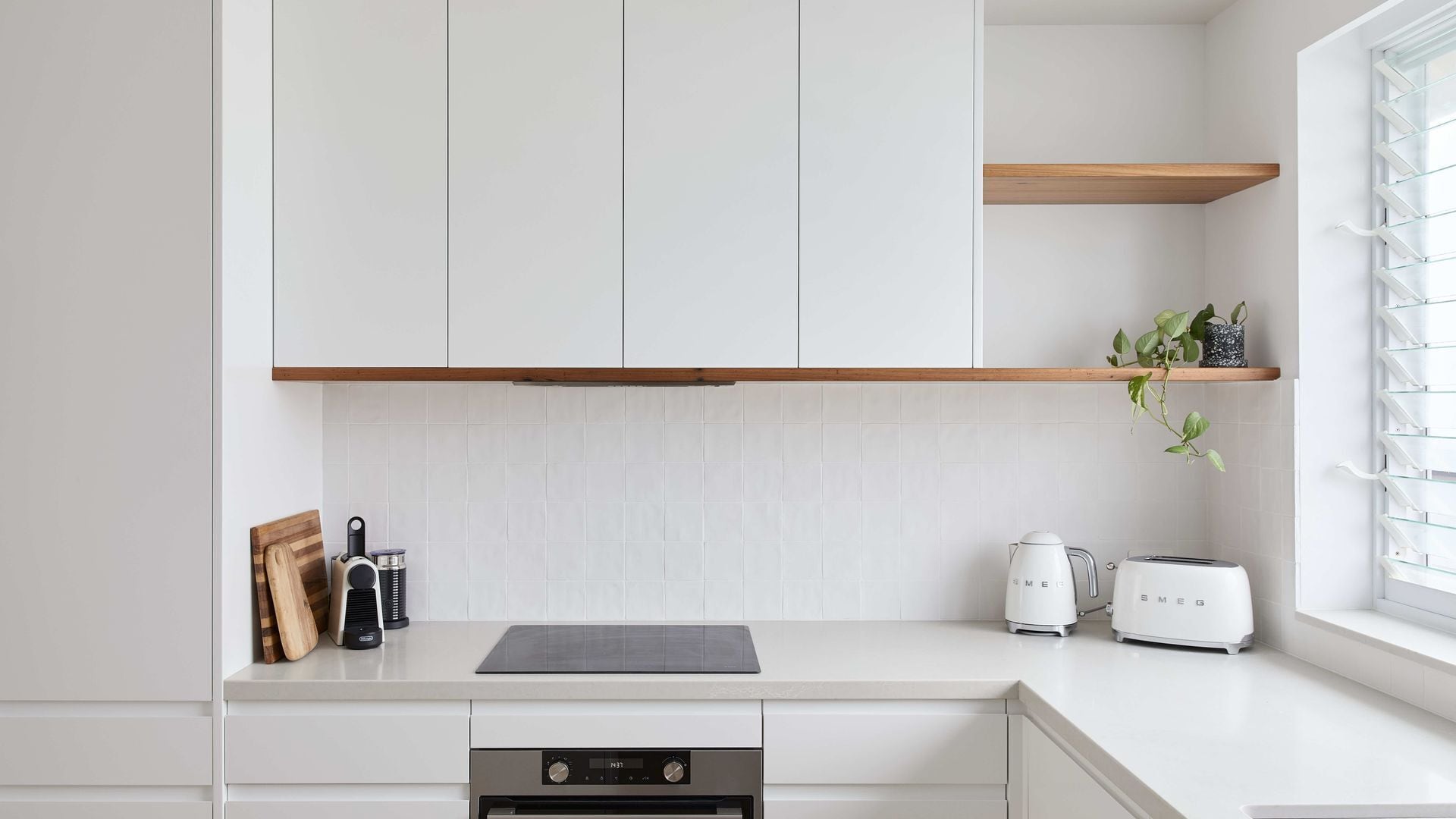 Une cuisine moderne avec des meubles blancs, un plan de travail en bois, un four encastré, une bouilloire et un grille-pain.