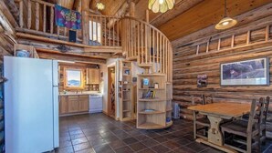 Interior rústico de una cabaña con cocina, comedor y una escalera en espiral.