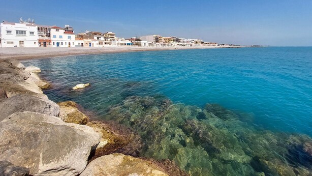Une ville côtière avec des bâtiments qui bordent le front de mer, une mer d’un bleu limpide et une côte rocheuse.