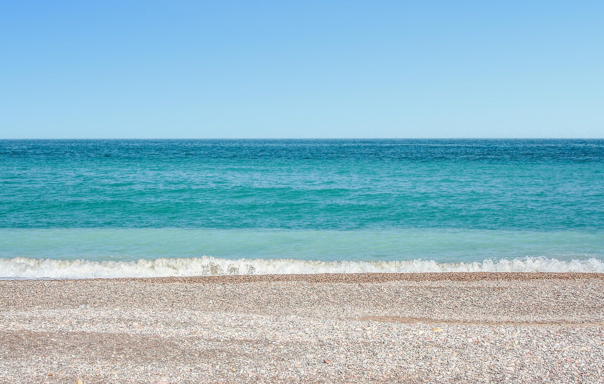 Une plage de galets bordée d’une eau turquoise et limpide, et une mer calme.