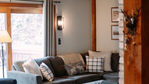 Ein gemütliches Wohnzimmer mit Holzboden, Kamin und großem Fenster mit Vorhängen.