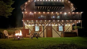 Eine zweigeschossige Holzhütte mit Balkon, Feuerstelle und Sitzgelegenheit im Freien.