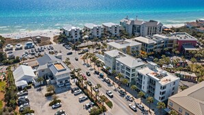 Vue aérienne d’un complexe hôtelier situé sur la côte, avec plusieurs bâtiments, un parking et une plage en arrière-plan.
