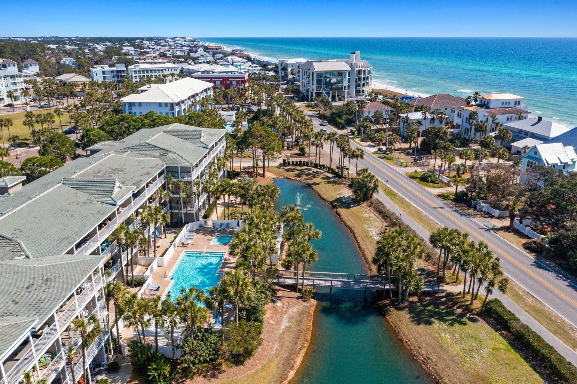 Vista aerea di un resort costiero con piscina, palme e un ponte su un canale d'acqua.