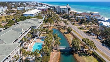 Luftaufnahme eines Küstenresorts mit Schwimmbad, Palmen und einer Brücke über einen Wasserkanal.