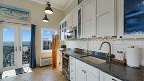 A modern kitchen with white cabinets, a granite countertop, stainless steel appliances, and a view of the ocean through a large window. - WOW! Water View Corner Unit, Free Wine + Bottled Water Arrival Gift (Santa Rosa Beach)