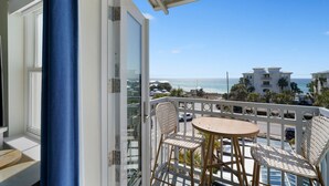 A balcony with wicker chairs and a small round table, overlooking a beach with buildings and palm trees. - WOW! Water View Corner Unit, Free Wine + Bottled Water Arrival Gift (Santa Rosa Beach)